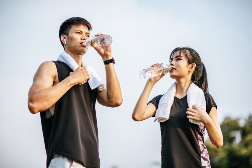 Men and women stand to drink water after exercise. Hydration vs recovery drinks
